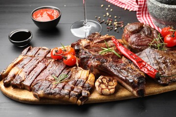 Pieces of tasty grilled beef with rosemary and vegetables on black wooden table, closeup