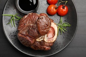 Tasty grilled beef steak served with rosemary, sauce and tomatoes on black wooden table, top view