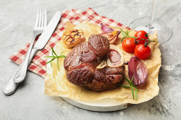 Tasty cut beef steak served with rosemary, garlic and tomatoes on grey textured table, closeup