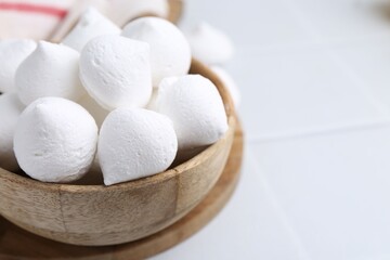 Delicious meringue cookies in bowl on white tiled table, closeup. Space for text