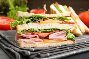Tasty sandwiches with ham, bacon, cheese and vegetables on black wooden table, closeup