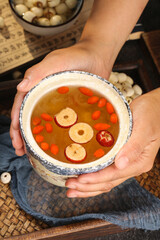 Hands holding traditional Chinese herbal soup with lotus seeds and red dates in ceramic bowl