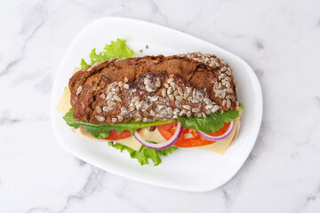 Tasty ciabatta sandwich with cheese and vegetables on white marble table, top view