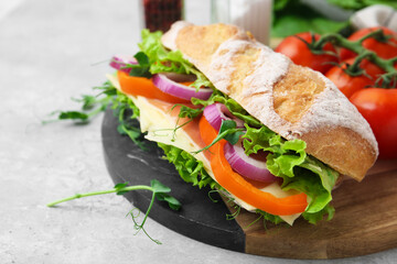 Delicious ciabatta sandwich with prosciutto, cheese and vegetables on light table, closeup