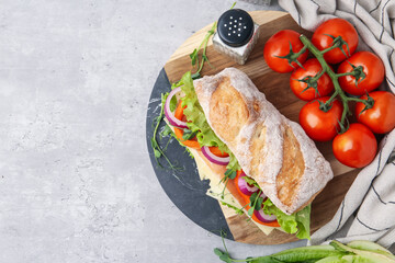 Delicious ciabatta sandwich with prosciutto, cheese and vegetables on light grey table, flat lay. Space for text