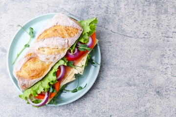Delicious ciabatta sandwich with prosciutto, cheese and vegetables on light grey table, top view. Space for text