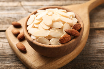 Fresh almond flakes and whole nuts in bowl on wooden table, closeup