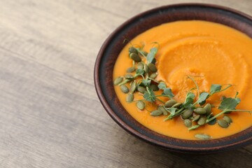 Delicious pumpkin soup with seeds and microgreens in bowl on wooden table, closeup. Space for text