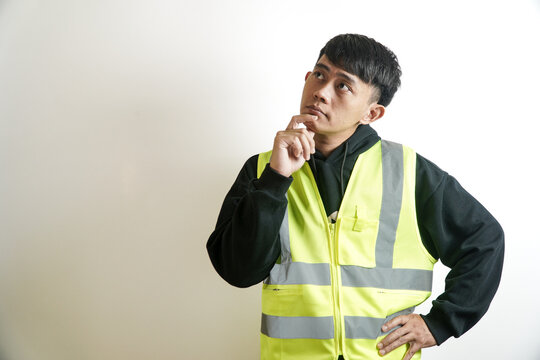 Portrait of a thoughtful young Asian construction worker in a reflective safety vest, contemplating a problem or planning a strategy against a neutral background