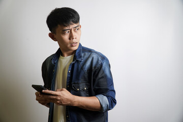 Stunned Asian man holding a smartphone looks away with a shocked and fearful expression after seeing something unexpected on his screen