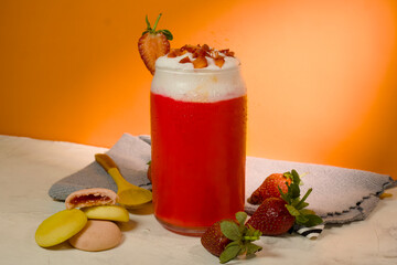 Cold strawberry juice with whipped cream topping and strawberry slices stands on white table