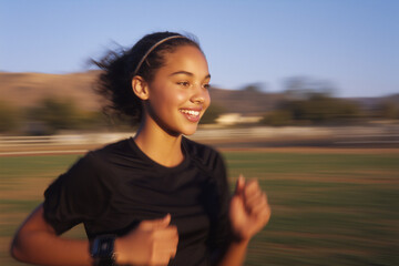 Happy teenager jogging in a park. Smiling young mixed race teenage girl exercising and wearing sportswear outdoors. School student being fit and active, fun fitness for young people	

