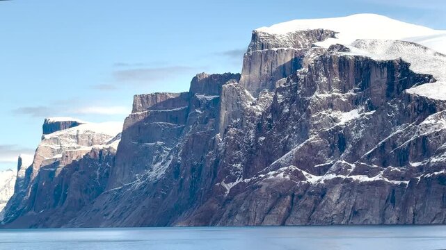 Witness the magnificence of Baffin Island coastal landscapes. The video captures impressive cliffs rising above calm blue waters, highlighting nature's raw beauty in a remote region.