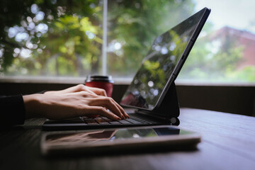 Close-up of a person typing on a laptop keyboard while holding a red coffee cup, working in a cozy...