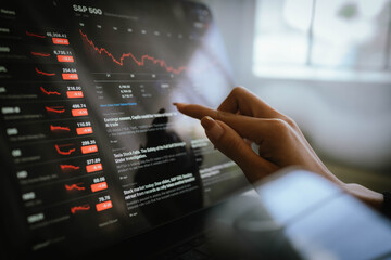 Hand using digital pen on tablet displaying stock market data and falling financial charts, representing trading analysis and investment monitoring.