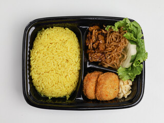 Nasi Kuning or saffron rice served with fried noodle, chicken nuggets, cucumber and lettuce