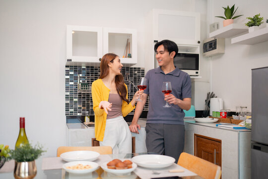 Adult Asian couple happily enjoying wine conversation modern kitchen home intimate moment shared casual evening relaxation together meal preparation romance