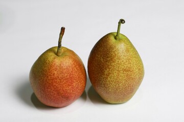 Two fresh pears with red, yellow, and green skin, and natural spots, placed on a clean white surface