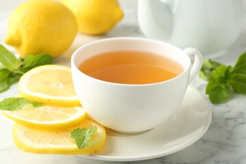 Aromatic tea in cup with lemons and mint on white marble table, closeup
