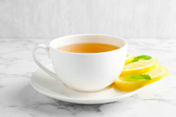 Aromatic tea in cup with lemon and mint on white marble table, closeup