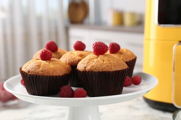 Freshly baked muffins with raspberries and air fryer on table in kitchen, closeup