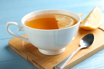 Aromatic tea in cup with lemon and spoon on light blue wooden table, closeup