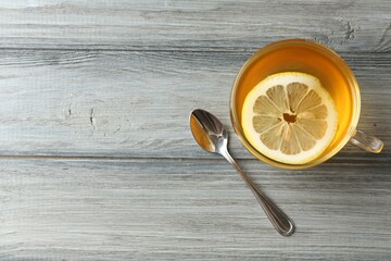 Aromatic tea with lemon in cup and spoon on wooden table, flat lay. Space for text