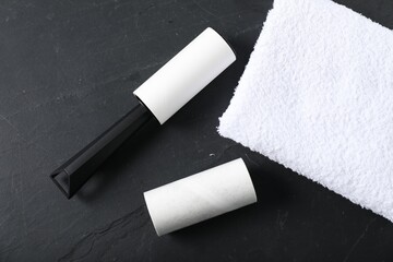Lint roller, adhesive roll and towel on black table, flat lay