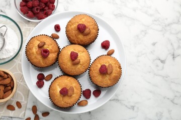 Fresh muffins with raspberries, almonds and flour on white marble table, flat lay. Space for text