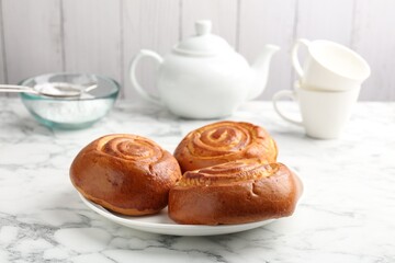Tasty roll buns, cups, teapot and flour on white marble table, closeup
