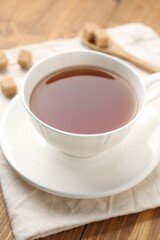 Aromatic black tea in cup and sugar cubes on wooden table, closeup