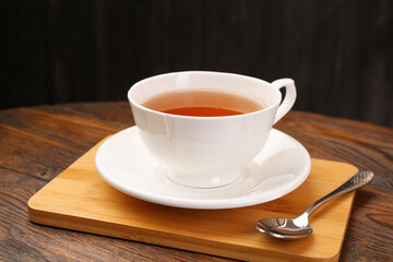 Aromatic black tea in cup and spoon on wooden table, closeup