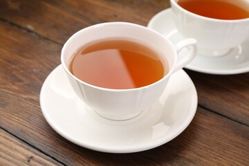 Aromatic black tea in cups on wooden table, closeup