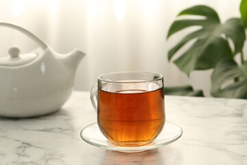 Aromatic black tea in glass cup and teapot on white marble table, closeup