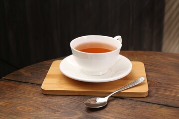Aromatic black tea in cup and spoon on wooden table, closeup