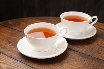 Aromatic black tea in cups on wooden table, closeup