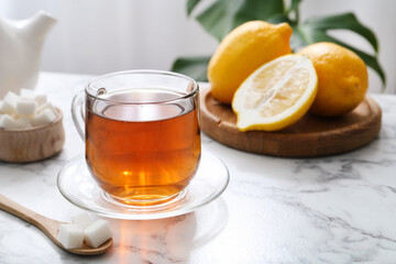 Aromatic black tea in glass cup, sugar and lemons on white marble table, closeup