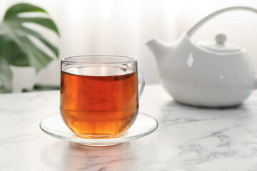 Aromatic black tea in glass cup and teapot on white marble table, closeup. Space for text