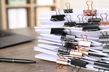 Many documents with binder clips and pen on wooden desk, closeup