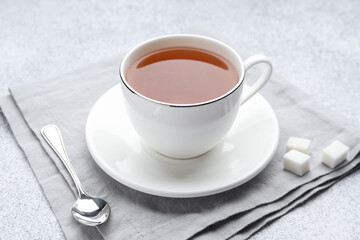 Aromatic black tea in cup, sugar and spoon on light grey table, closeup