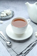Aromatic black tea in cup, sugar, teapot and spoon on light grey table, closeup
