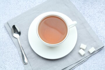 Aromatic black tea in cup, sugar and spoon on light grey table, flat lay