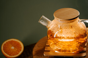 Warm green tea kettle steaming beside fresh orange on a wooden table in calming setting