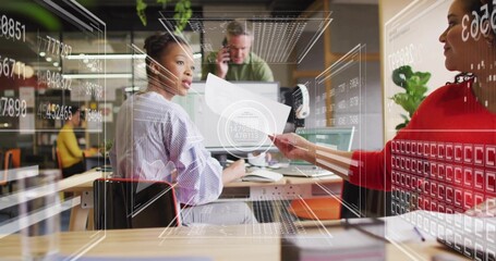 Collaborating woman in striped top holding page turning to colleague at office desk, data overlays