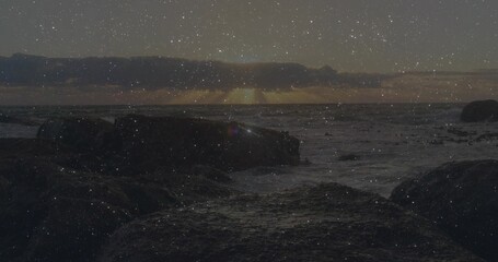 Sun sinking over horizon, casting glow on ocean waves crashing on rocky seashore under cloud layer