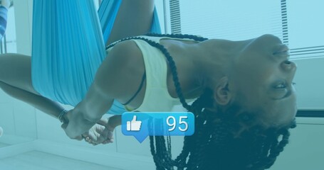 Hanging woman in tank top doing aerial yoga inversion in studio with blue hammock thumbs-up overlay