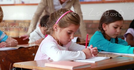 Writing child girl with pink headband at wooden classroom desk, teacher observing and math formulas
