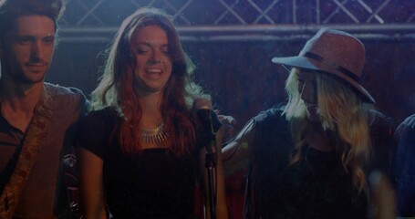 Singing bandmates on stage near metal truss, holding microphone and playing guitar under lights