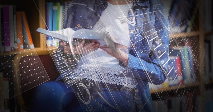 Reading teenage student holding hardback book in library seating area, with holographic charts