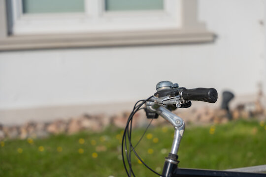 Close-up of a bicycle handlebar with bell and brake lever. The focus lies on the shiny metal and rubber grip.